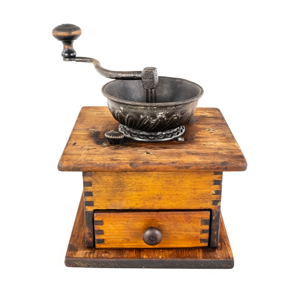 Antique Box-Style Manual Coffee Grinder: Antique Box-Style Manual Coffee Grinder, cast iron hopper sits on a wooden box, long crank handle rotates an internal iron burr to crush the beans, grounds drop directly into a small drawer at the fro