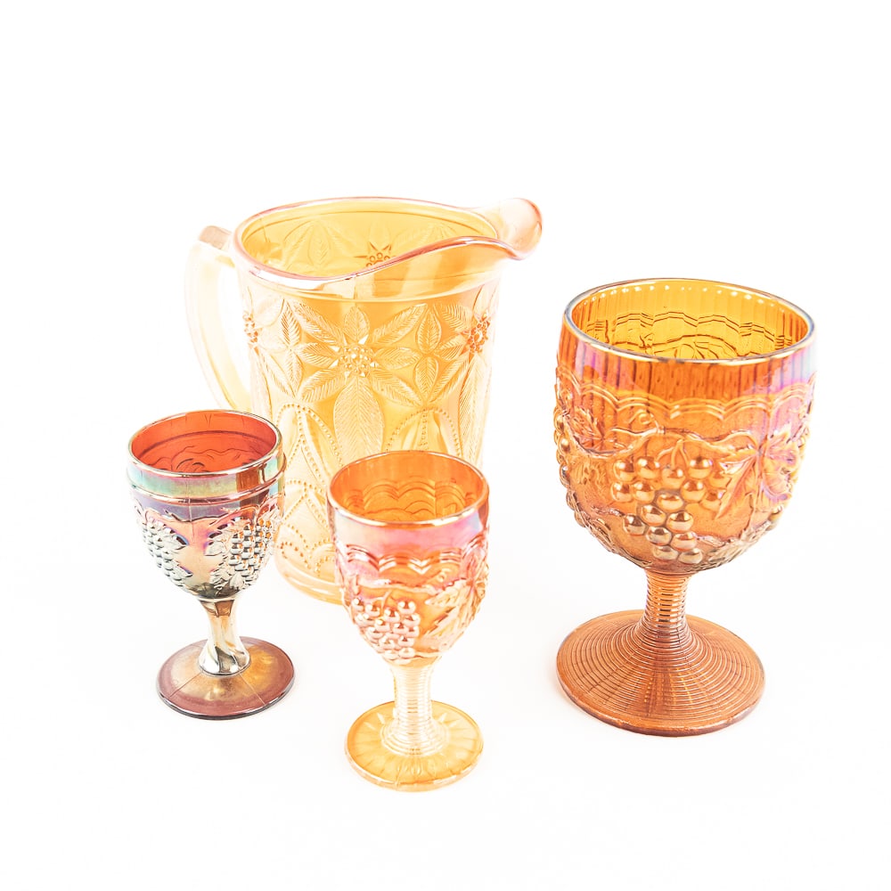 Carnival Glass: Assortment 4-Pc Lot: 4-piece lot. Imperial Grape goblet in amber (5 3/4 in tall). Imperial Grape wine in marigold. Dugan Vintage wine in amethyst. Imperial Poinsettia milk pitcher in marigold (6 1/4 in tall). All items ar