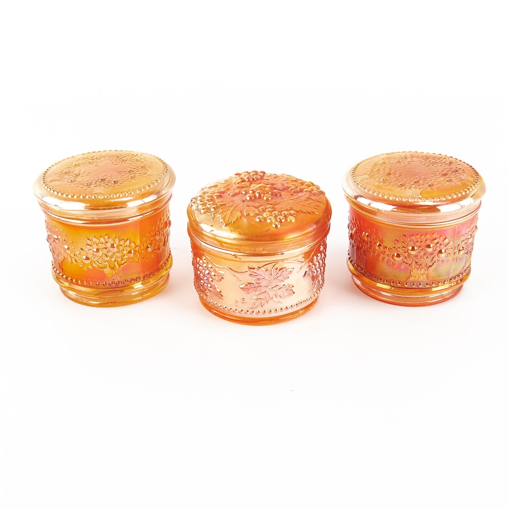 Carnival Glass Covered Powder Jars: 3-Pc Lot: All marigold. Includes two Fenton Orange Tree powder jars and one Dugan Vintage jar. Condition is good other than typical chips underneath the lids on all three.See photos to judge condition and bid a