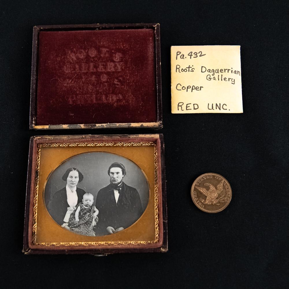 1/6 Plate Root Daguerreotype W Token: Cased 1/6 plate horizontal Dag of a seated husband, wife, and child with an oval matte mounted in a Root's Gallery leatherette case with detached hinge. Image in VG condition. Resealed with archival