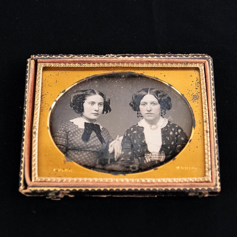 1/4 Plate Dagguereotype of 2 ID'd Women: 1/4 plate horizontal hand tinted Daguerreotype of 2 women mounted with an oval matte in a case with missing cover. The matte is stamped G. Page Meriden. Page operated a studio in Meriden Connecticut