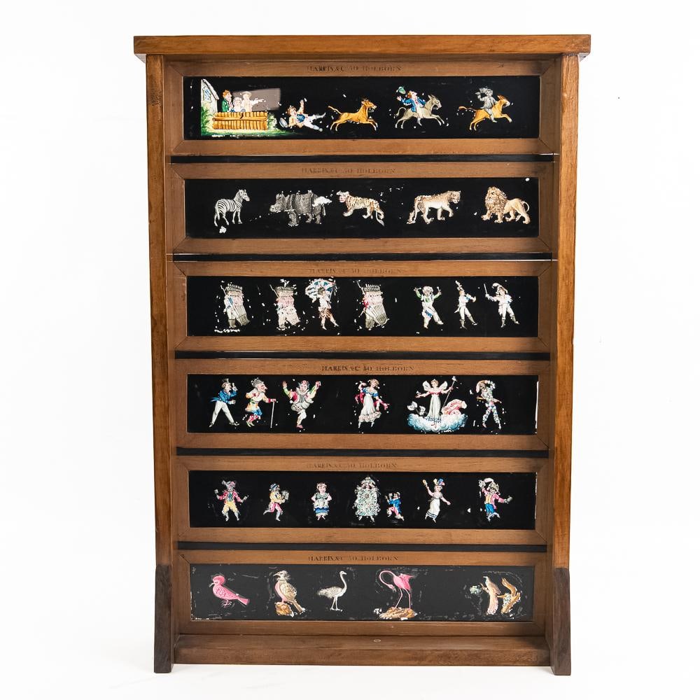 Harris & Co. Magic Lantern Slide Display: This custom wooden display stand features six tiers showcasing a collection of hand-painted magic lantern glass slides. Dating to the late 19th or early 20th century, pieces originating from the