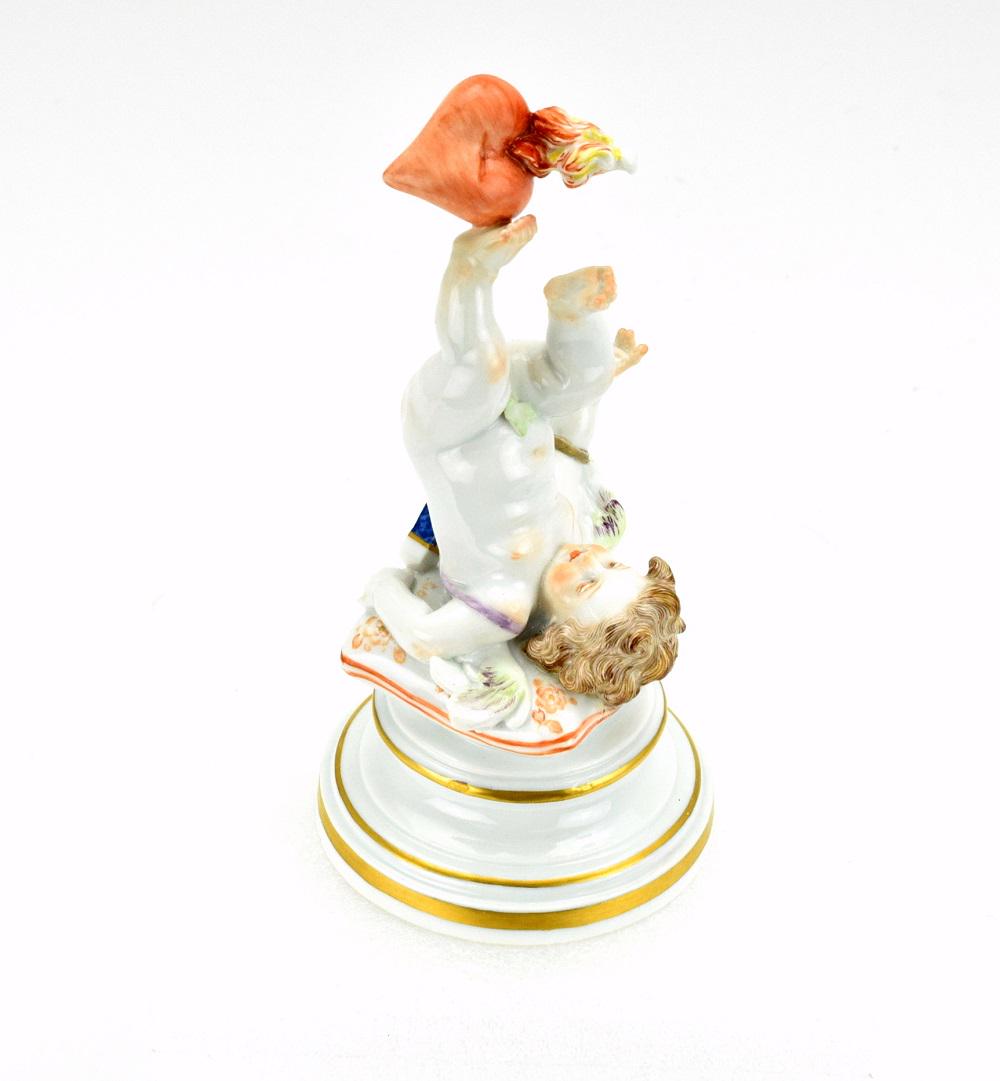 ANTIQUE MEISSEN PORCELAIN FIGURINE CHERUB CUPID WITH: Antique Meissen porcelain cherub laying on his back and holding a heart on his foot. 7" height. Marked on base.Very fine quality and details.