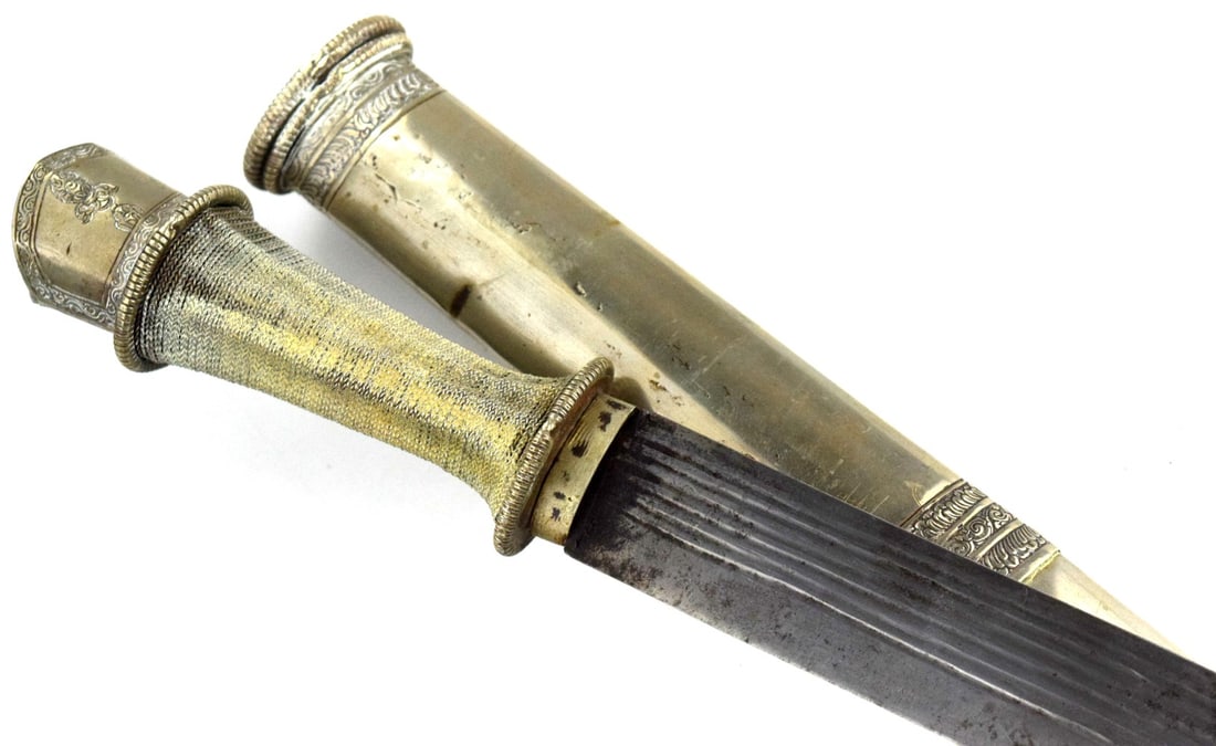 Good 19th Century Tibetan or Bhutanese Sword: The hilt is a classic Tibetan form, with a distinctive trefoil (three-lobed) pommel and a grip that is tightly wrapped in wire, likely silver or a silver alloy. It also features an oval guard.Blade: T