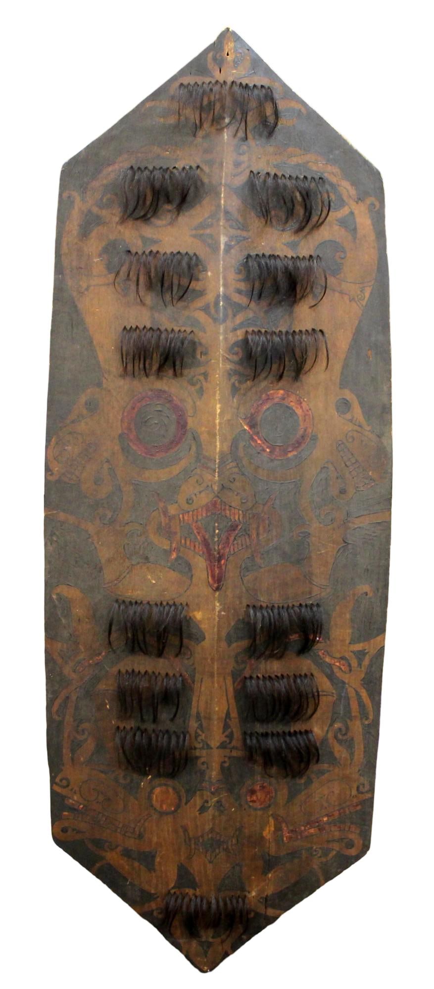 Rare Late 19th-early 20th c Dayak Kilau (or kelebit) Sheild: Of characteristic form, carved from a single large section of wood with raised central ridge and integral grip to the reverse and elaborately embellished with numerous hair tassels. Both the obverse a