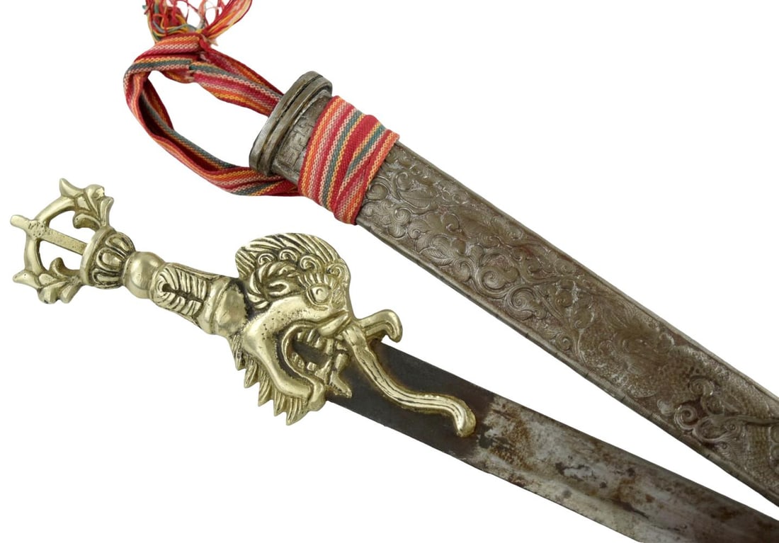 19th Century Tibetan or Himalayan Sword with Gilt-Brass Makara Hilt and Repouss Scabbard: A distinctive 19th century Tibetan or Himalayan sword, fitted with an elaborate cast and chased brass hilt incorporating a fierce makara or dragon-like zoomorphic mask, its open jaws embracing the bas