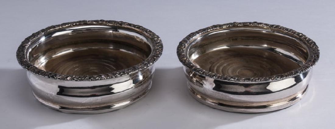 (2) Silverplate and wood wine bottle coasters, 6"dia: Pair of silverplate and wood wine bottle coasters, having flattened repousse' rims above undulating bodies, with wooden bottoms, apparently unmarked, 2"h x 6"dia.