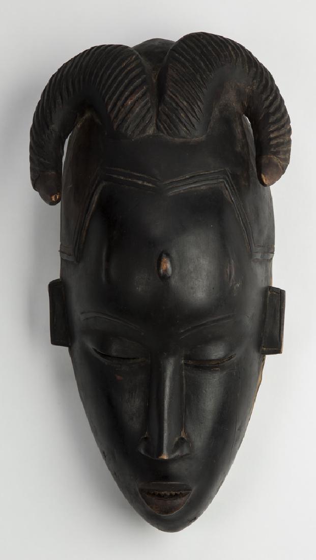 West African Baule style wooden mask, 13"h: West African Baule style carved and ebonized wooden mask, having a stylized face, with a rounded forehead with arched eyebrows, nearly closed almond-shaped eyes, elongated sculpted nose, and a partial