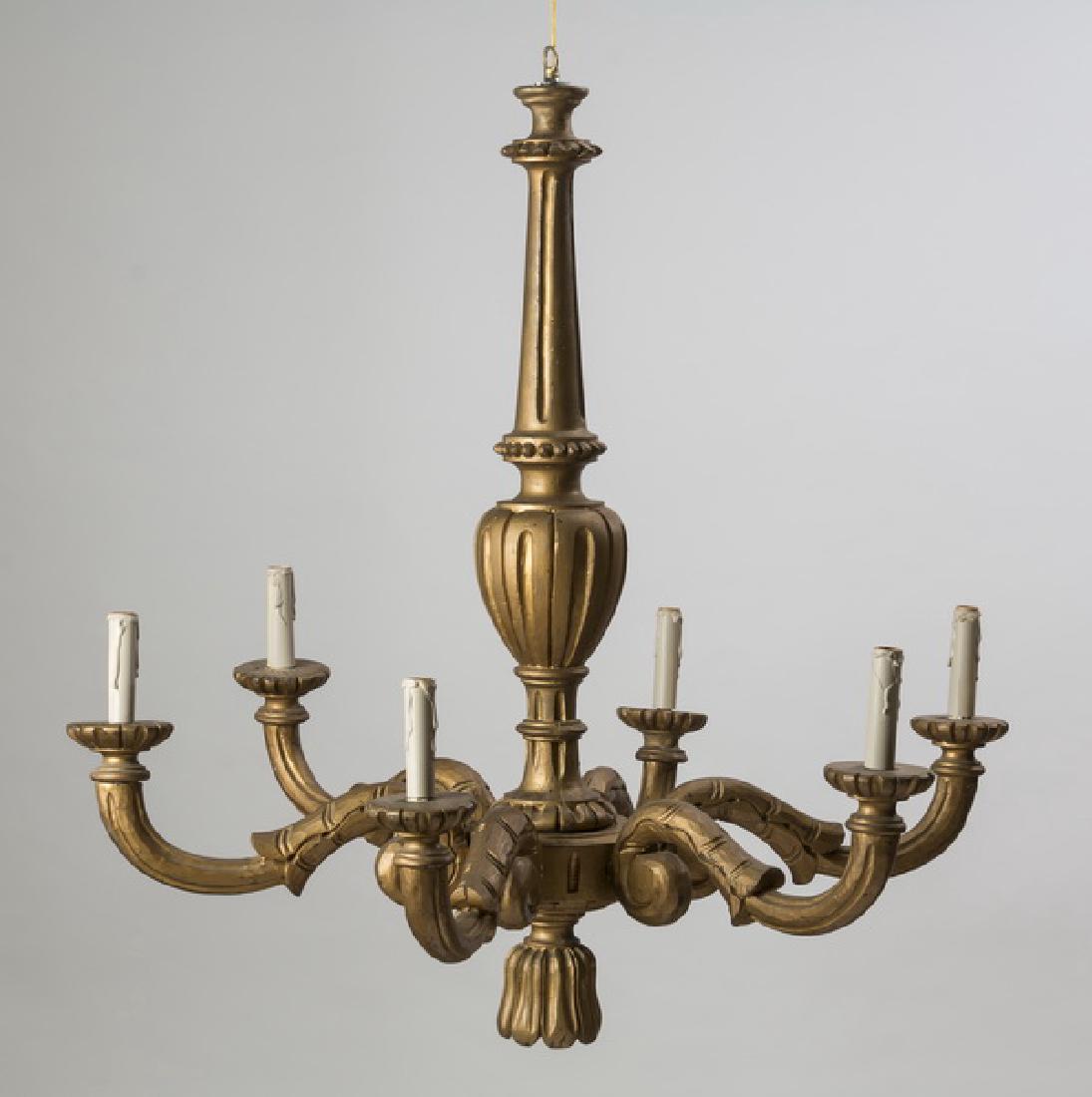 Gilded 6-arm carved wood chandelier, 32"h: Gilded six arm carved wood chandelier, having a fluted tapering neck, surmounting a baluster standard, issuing six 'S' scroll arms, ending in bobeches, above a tassel pendant, 32"h x 33"dia.