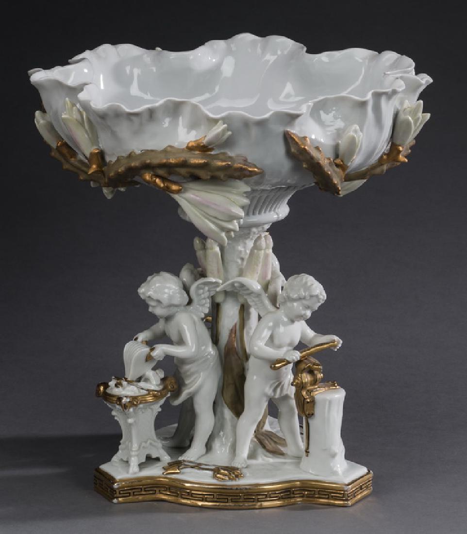 Continental porcelain putti centerpiece, 12"h: Continental parcel gilt and blanc de chine porcelain centerpiece in the Rococo taste, having a petal form bowl with applied gilt foliage, surmounting a columnar standard surrounded by three putti indu