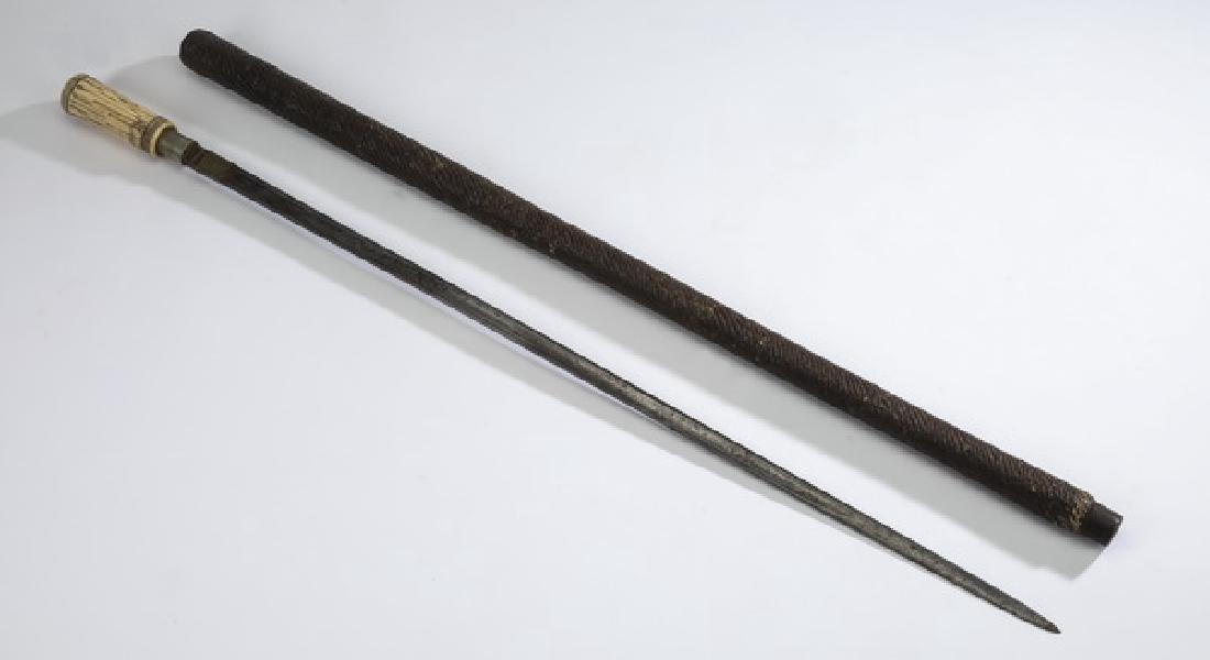 Bone and wood sword cane, 35"l: Bone and wood sword cane, having a carved bone columnar knob handle, above a wide wooden shaft with carved texture ending in a metal ferrule, the sword having a single fuller on each side, blade 28.25