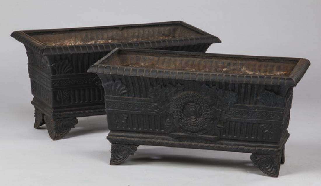 (2) Cast iron jardinieres in the French taste, 28"w: Pair of rectangular cast iron jardinieres in the French taste, having gadrooned rims above bodies featuring decorative Neoclassical designs on opposing sides, centering relief molded wreaths surrounde