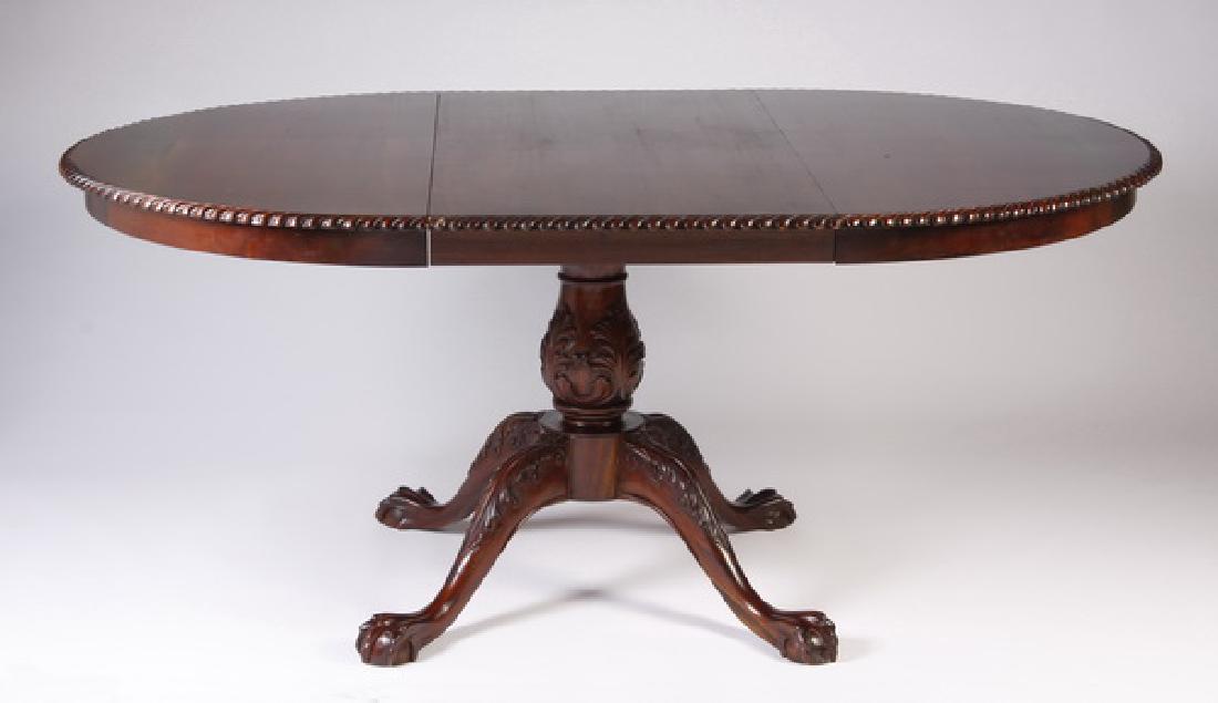 Chippendale style mahogany dining table: 20th century Chippendale style carved mahogany dining table with additional leaf, the round top with gadrooning at the verge, the base with a foliate adorned baluster form standard raised on four legs