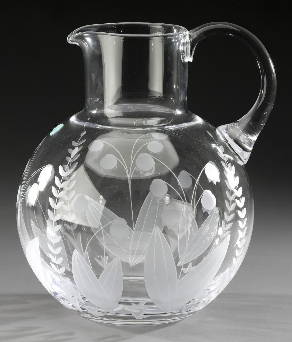 Tiffany & Co crystal 'Lily of the Valley' pitcher: Tiffany & Co. hand blown crystal pitcher in the 'Lily of the Valley' pattern, having a circular opening with spout, issuing a side handle connected to the globular pitcher, etched throughout in a lily
