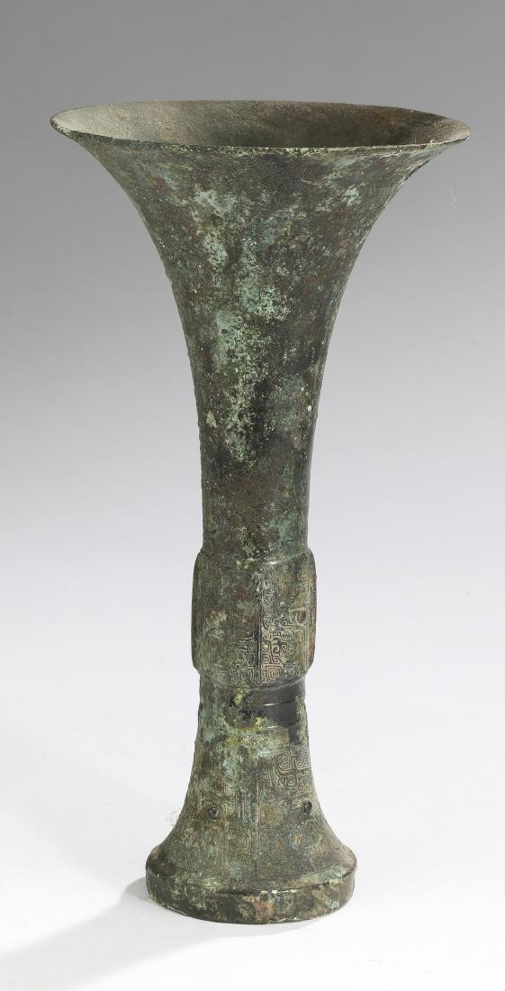 Chinese bronze Gu, possibly Shang Dynasty, 11"h: Chinese bronze Gu vase, possibly Shang Dynasty, 1766-1046 BC, having a trumpet neck, above a concave body with a band of incised taotie masks divided by the vestiges of four flanges, the whole rising 