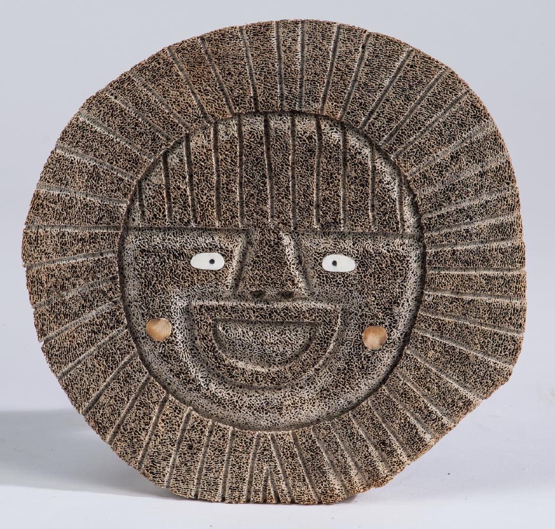 Inuit whale bone spirit mask, signed, 8"dia: Inuit whale bone spirit mask, depicting a face, having inlaid eyes and cheeks with a wide smile radiating linear beams, signed indistinctly by artist on the back, 0.75"h x 8"dia.