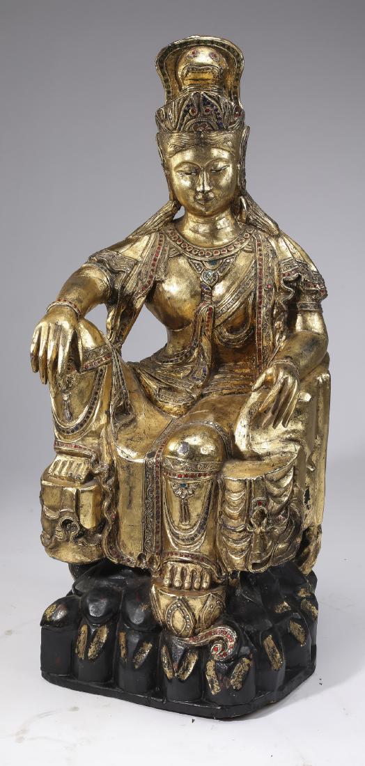 Gilded and carved wood Guanyin, 41"h: Gilded and carved wood Guanyin, depicting a seated goddess of mercy gilded throughout and accented with scarlet, sapphire, and ruby sequins, seated on a gilded throne, the whole resting on a shaped lo