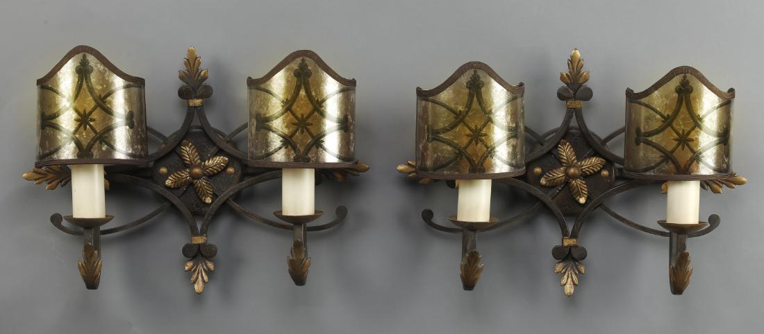 (2) Gilded iron wall sconces w/ faux mica shades: Pair of Spanish Renaissance Revival style 2-light wall sconces, each having a circular iron wall mount with a central gilded foliate accent bordered in a diamond form with gilded leaf accents at the c
