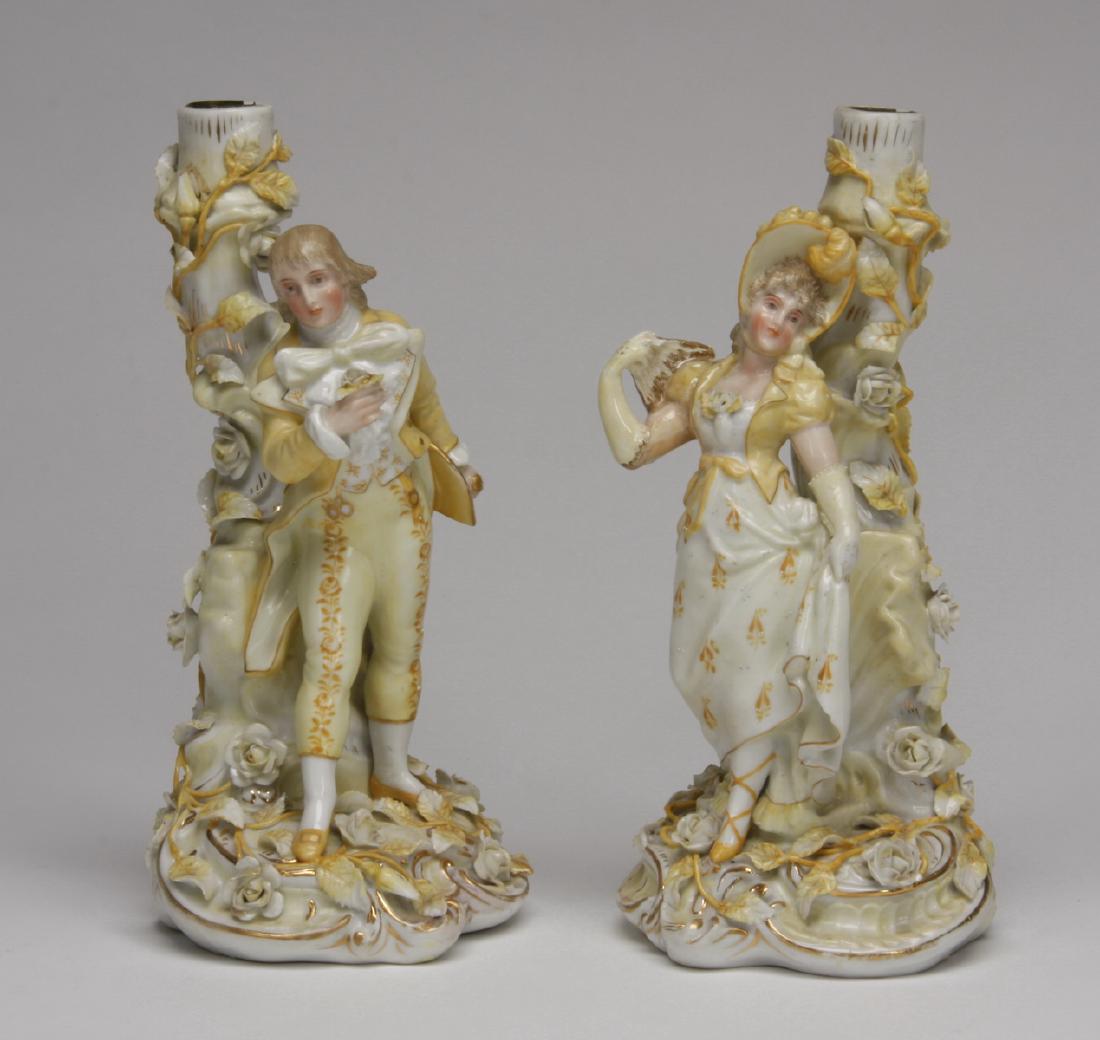 Late 19th c. Sitzendorf figural candleholders: Pair of late 19th or early 20th century German porcelain candleholders, in the form of a man and maiden in period dress, against stylized tree trunks encircled with climbing roses, on an asymmetrical 