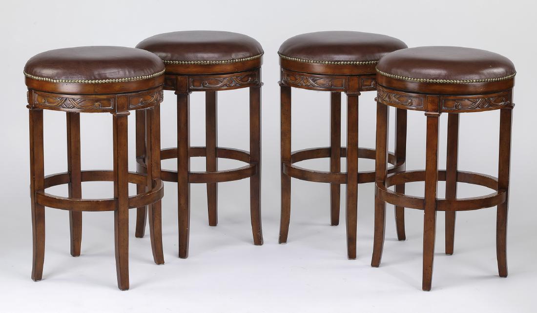(4) Leather upholstered swivel bar stools, 30"h: Set of four traditional leather bar stools, each having a circular leather upholstered revolving seat with nail head trim, above an apron with relief carved scroll panels, the whole rising on square l