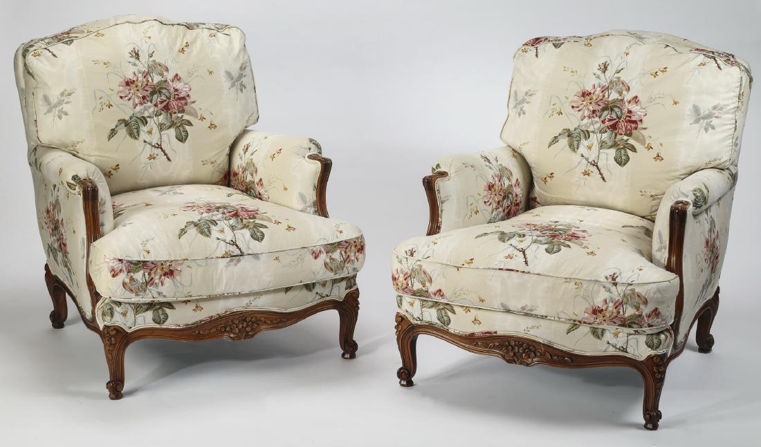 (2) Custom upholstered French walnut bergeres: Pair of French walnut bergeres, early 20th century, having tablet backs above rolled arms, flanking drop-in down filled back and seat cushions custom upholstered in rose and cream floral glazed cotton