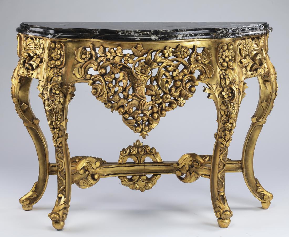 Italian marble & gilt wood demi-lune console: Italian marble and gilt wood demi-lune console in the Rococo taste, having a shaped black marble top above a wide gilt wood apron pierced and carved with foliate motifs, the whole rising on heavily ca