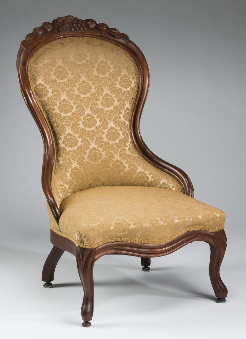 Victorian carved slipper chair, in gold damask: Victorian low slipper or parlor chair, the mahogany frame carved with central grape and fruit crest, the whole upholstered in gold damask and rising on two outswept and two cabriole legs terminating i