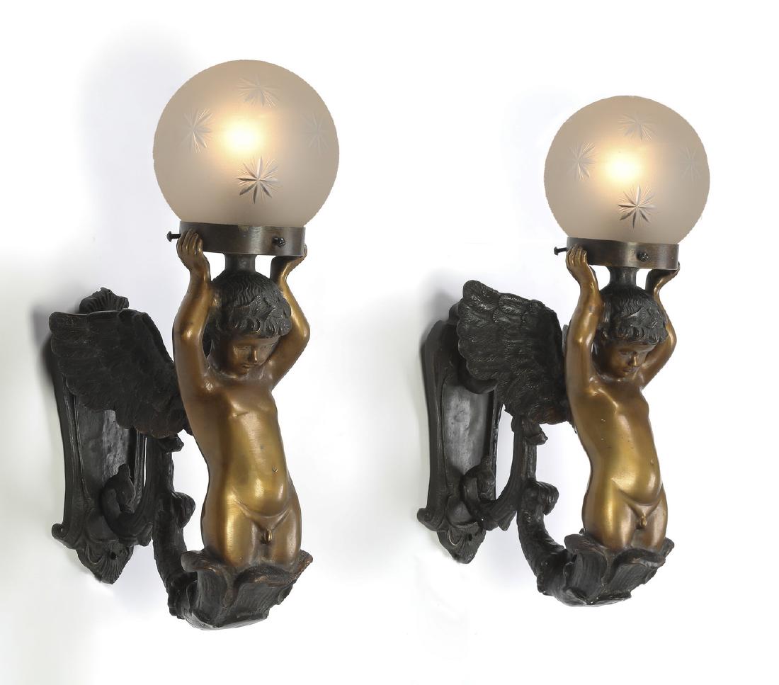 (2) Gilt and patinated bronze cherub wall sconces: Pair of gilt and patinated bronze cherub sconces, each having a shaped wall plate issuing a cornucopia from which a winged putto emerges lifting a bobeche over his head, supporting a spherical frosted