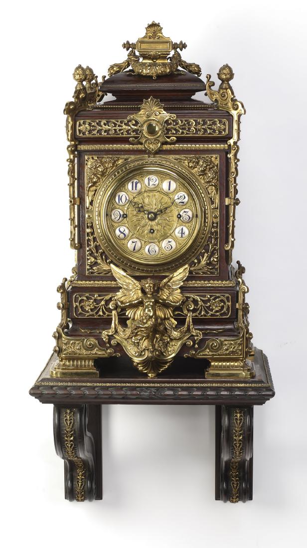 English bronze & oak bracket clock, ca 1850: English bronze and oak clock and wall bracket, circa 1850, the arched case with a hipped roof surmounted by a bronze ribbon bound wreath, the corners capped by pinecone finials above pierced and arche