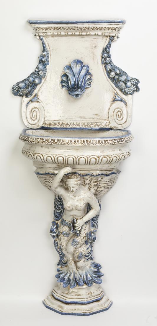 Continental majolica wall mounted fountain, 63"h: Continental majolica wall mounted fountain in the Neo-Classical taste, having an upper plaque centering a stylized dolphin head spigot, flanked by slate blue fruited swags, 23"h x 27"w; surmounting a 