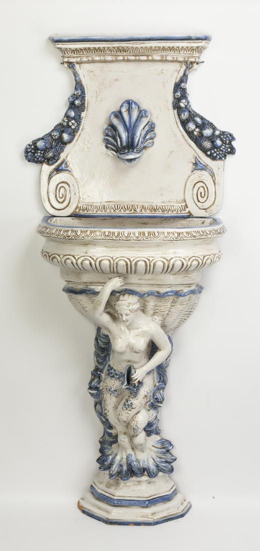 Continental majolica wall mounted fountain, 63"h: Continental majolica wall mounted fountain in the Neo-Classical taste, having an upper plaque centering a stylized dolphin head spigot, flanked by slate blue fruited swags, 23"h x 27"w; surmounting a 