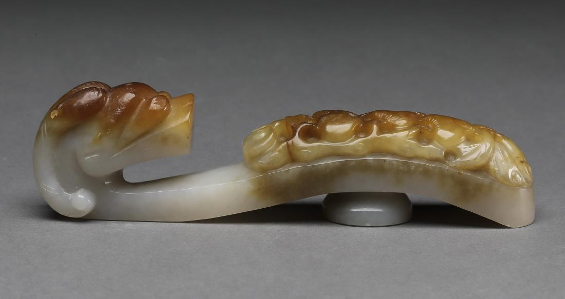 Chinese carved jade dragon belt buckle, 5"l: Chinese jade dragon belt buckle, executed in cream jade with russet inclusions, having a dragon head hook and a body pierce carved with lingzhi and fruit, 1"h x 4.5"l x 1"w.