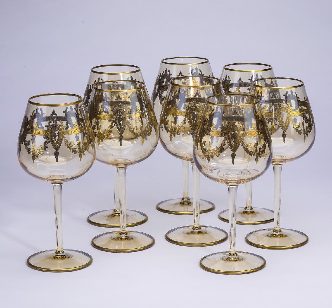 (8) Gilt decorated crystal red wine glasses: Set of (8) crystal red wine glasses, each having a gilt rim, with shields and swags below, rising on a cylindrical stem ending in a circular foot, 8.5"h x 4.5"d.