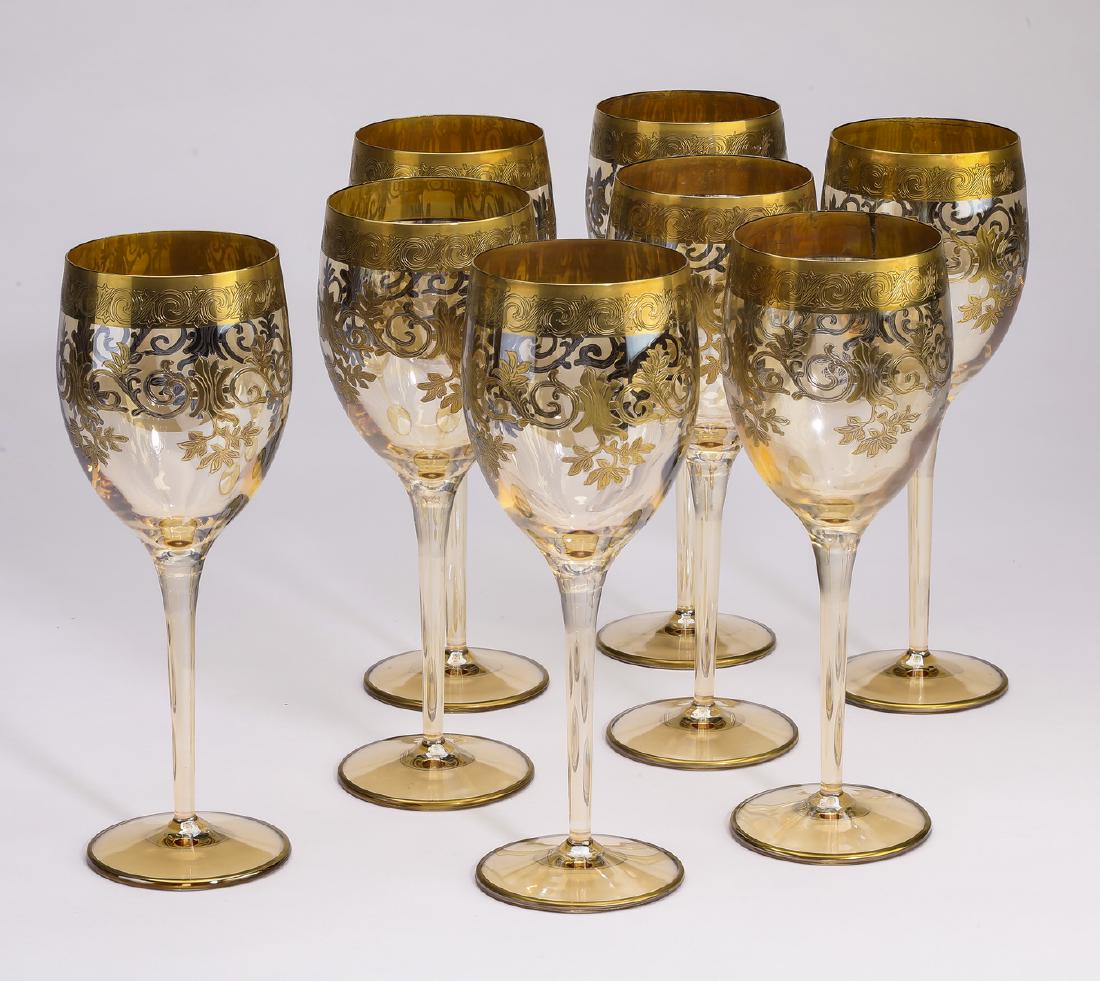 (8) Gilt decorated crystal white wine glasses: Set of (8) crystal white wine glasses, each having a gilt band around the rim, and repeating gilt folliate scrolls below, surmounting a cylindrical stem terminating to a circular foot, 9"h x 3.5"d.