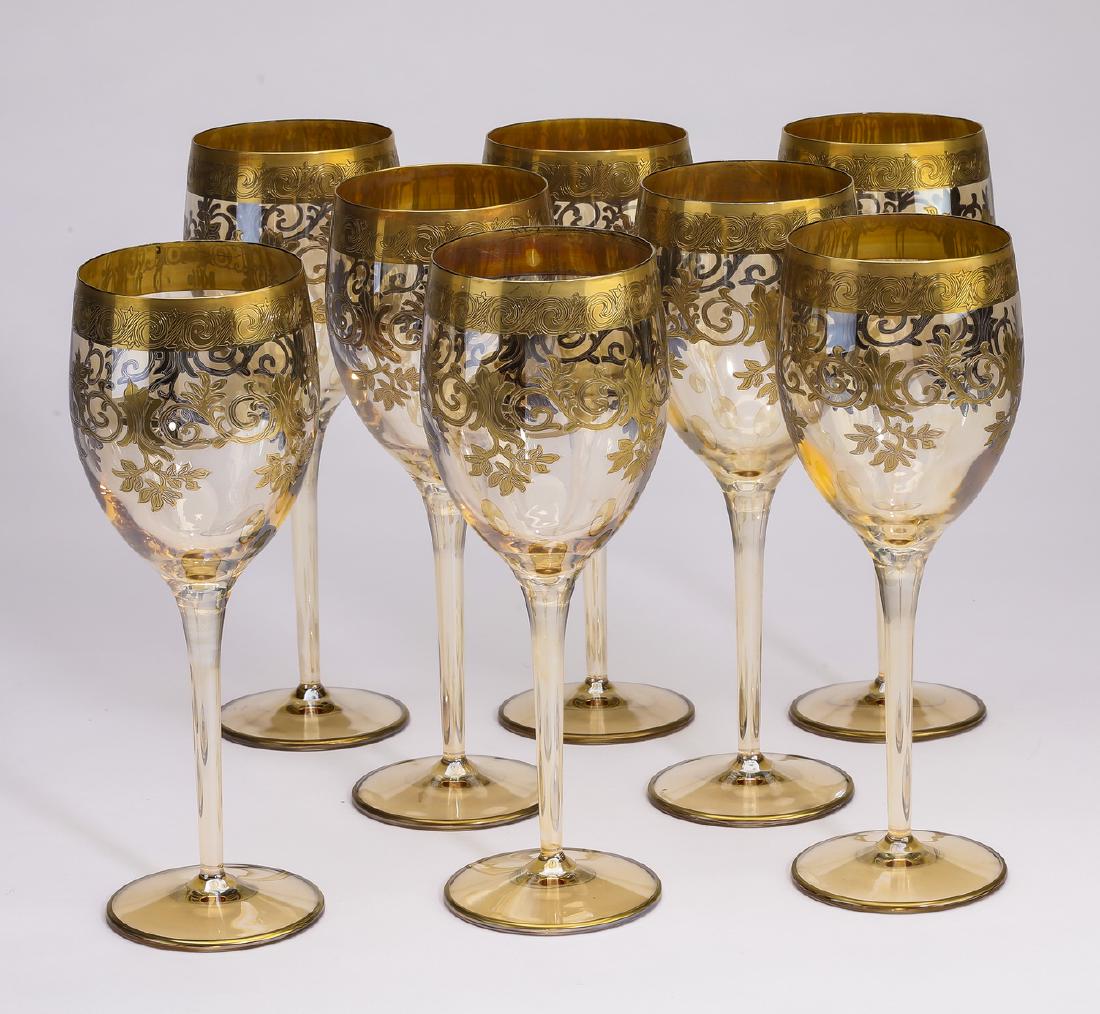 (8) Gilt decorated crystal white wine glasses: Set of (8) crystal white wine glasses, each having a gilt band around the rim, and repeating gilt folliate scrolls below, surmounting a cylindrical stem terminating to a circular foot, 9"h x 3.5"d.