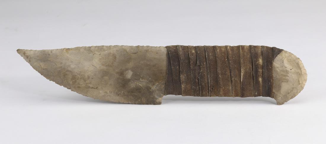 Flint knapped stone 'Bowie' knife, 10"l: Stone 'Bowie' knife, the flint knapped stone having a curved blade and an integral hilt wrapped in rawhide, 10.25"l x 2.25"w.