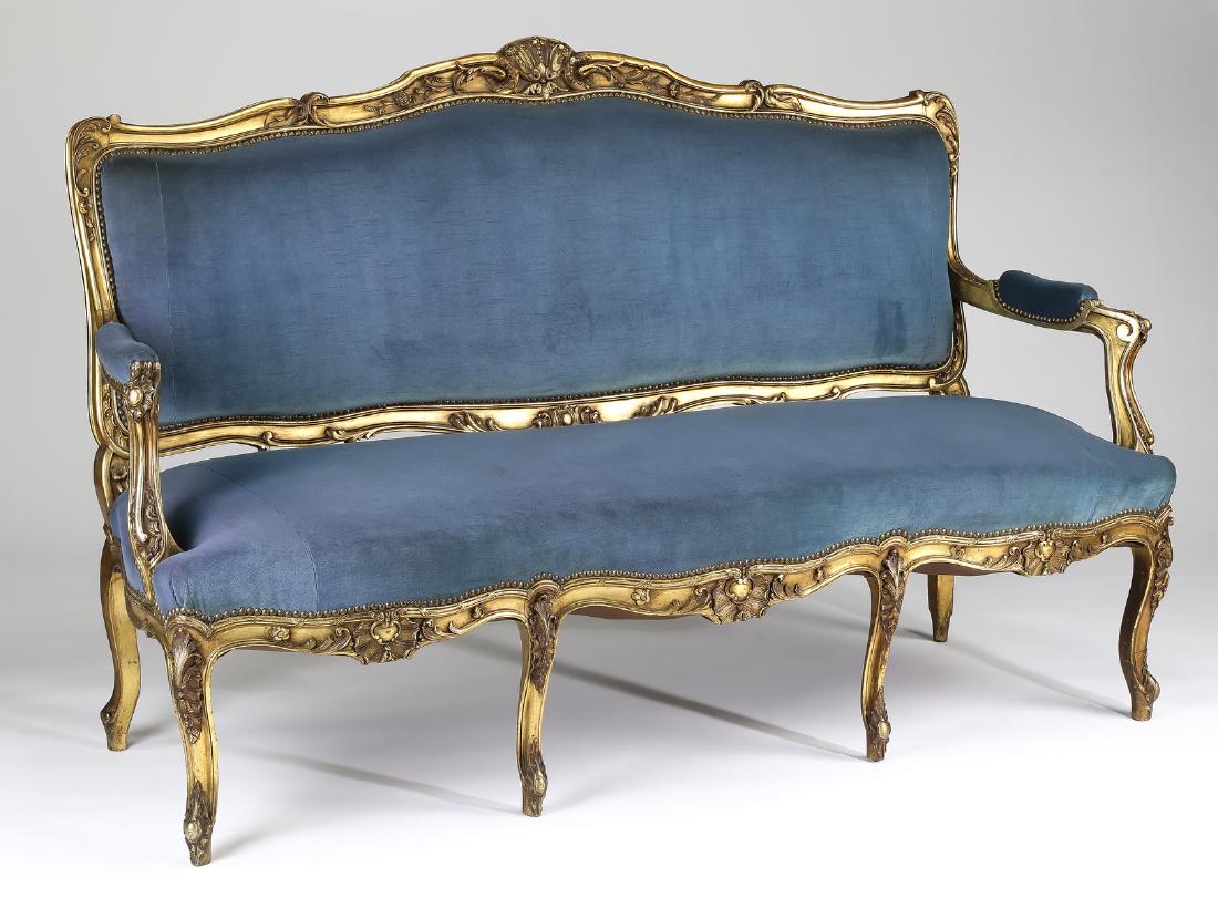 Early 20th c. French giltwood canape in velvet: Giltwood and velvet upholstered canape in the Louis XV taste, early 20th century, having a curving rectangular back with carved top and bottom rails, leading to partially upholstered arms, over a serp