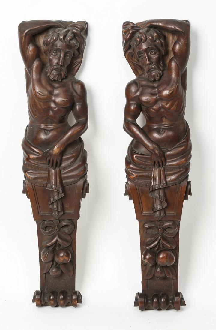 Pair of figural architectural elements, 22"h: Pair of figural architectural elements, each depicting a male term figure aurmounting bows and fruit, crafted of cast composite material. 21.5"h x 5"w x 2.25"d.