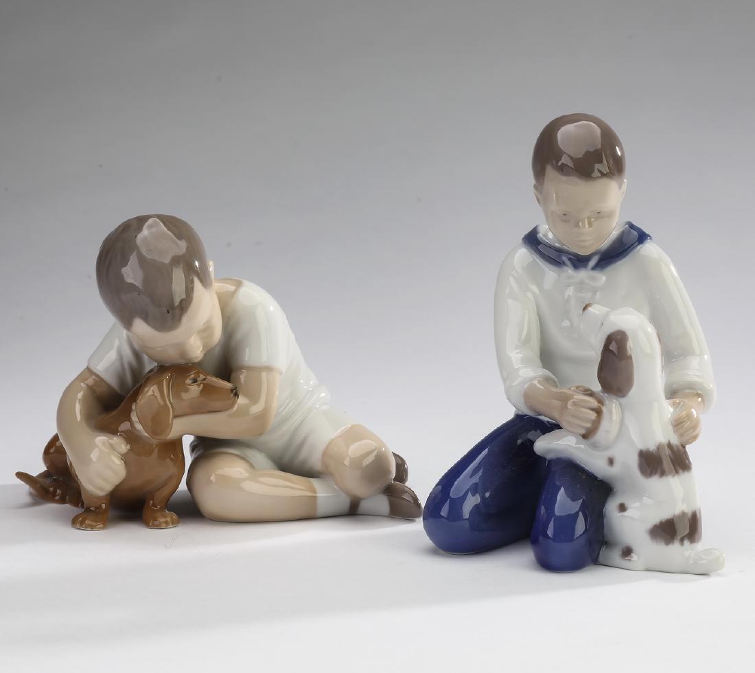 (2) Bing & Grondahl porcelain boys & puppies, 5"h: (2) Bing & Grondahl porcelain figures, comprising:#1951 'True Friendship' depicting a young boy embracing a small dog, 4"h x 5"w x 2.75"d; and #2334 'Grooming' depicting a boy brushing his dog, 5.25"h