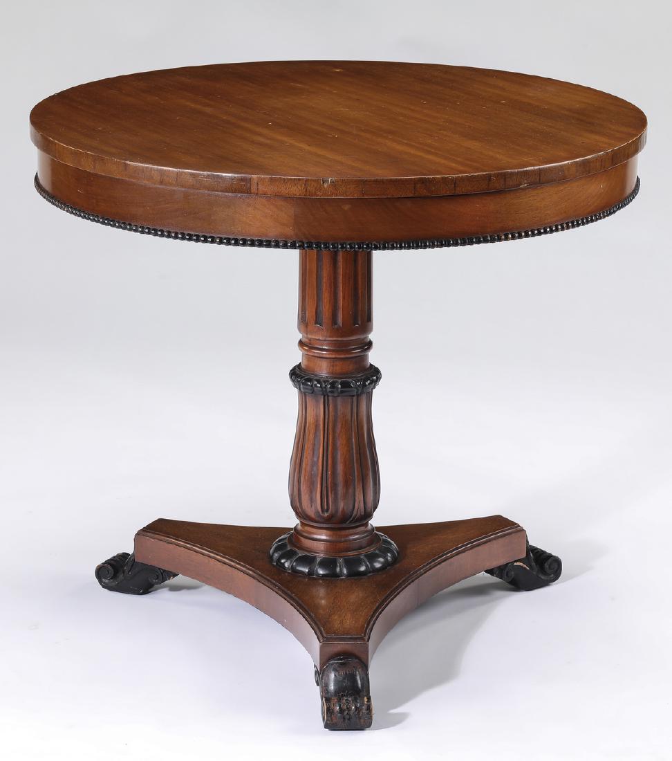 Mahogany and ebonized wood occasional table: Mahogany occasional table in the Neoclassical taste, having a round top above a wide apron with a gadrooned edge, rising on a reeded and fluted standard, resting on a triangular plinth ending in eboni