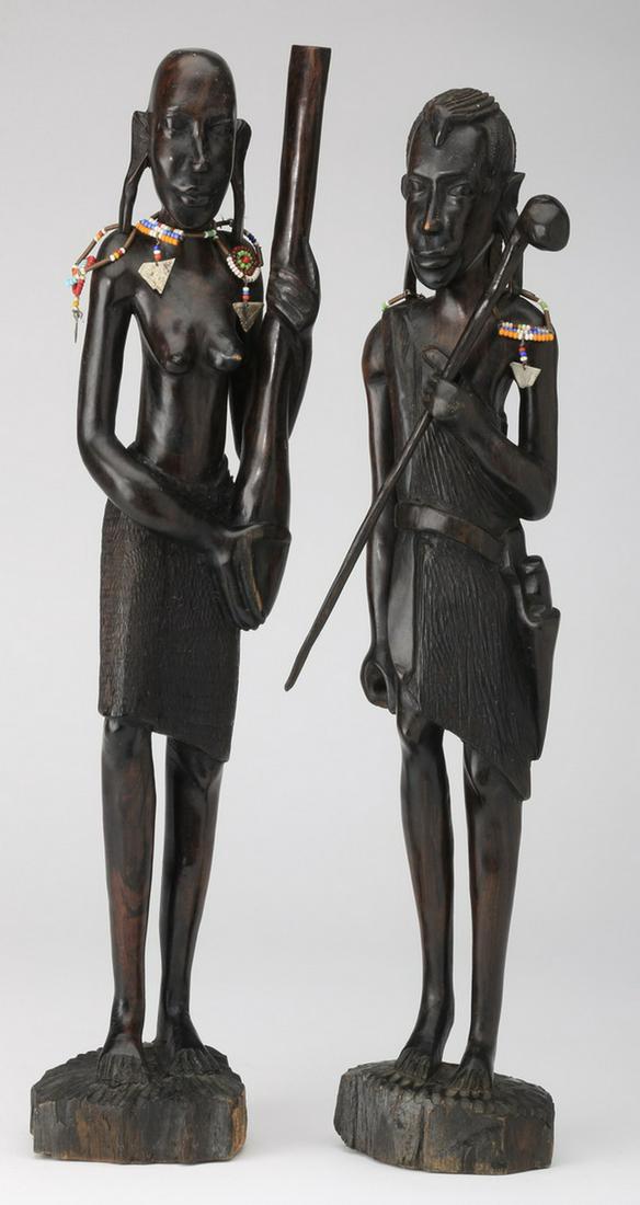 Pair of male and female carved ebony figures, 17"h: Pair of carved ebony male and female African figures, each holding a club/stick, and accented with beaded jewelry; female 16"h x 3.5"w x 2.5"d, male 17"h x 3.25"w x 2.5"d.