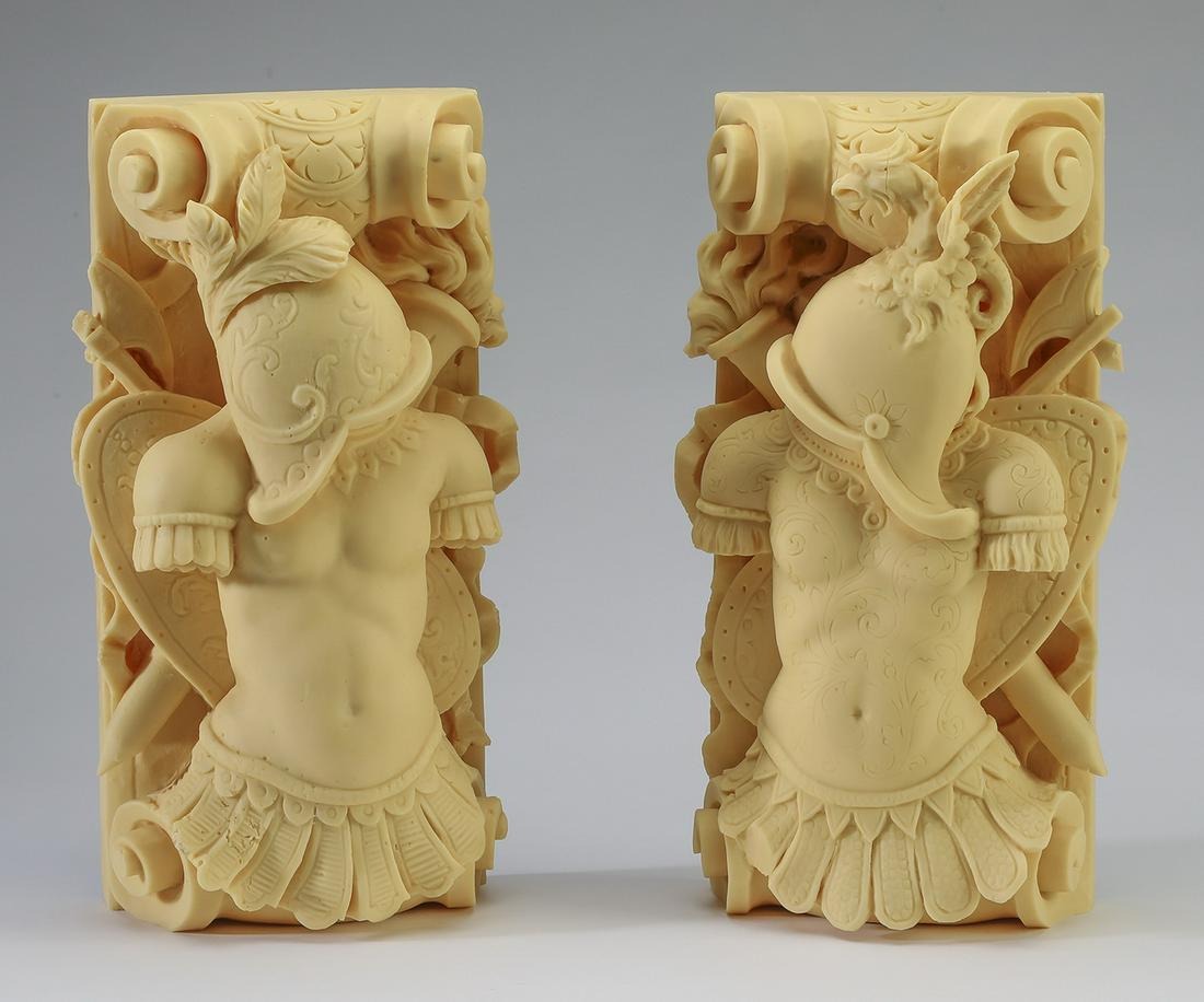 Pair of unfinished composite architectural elements: Pair of unfinished figural architectural elements, each having a C-scroll centering a dimensional crest depicting a feathered helmet and etched torso in front of a shield and axe crossed with a flamin