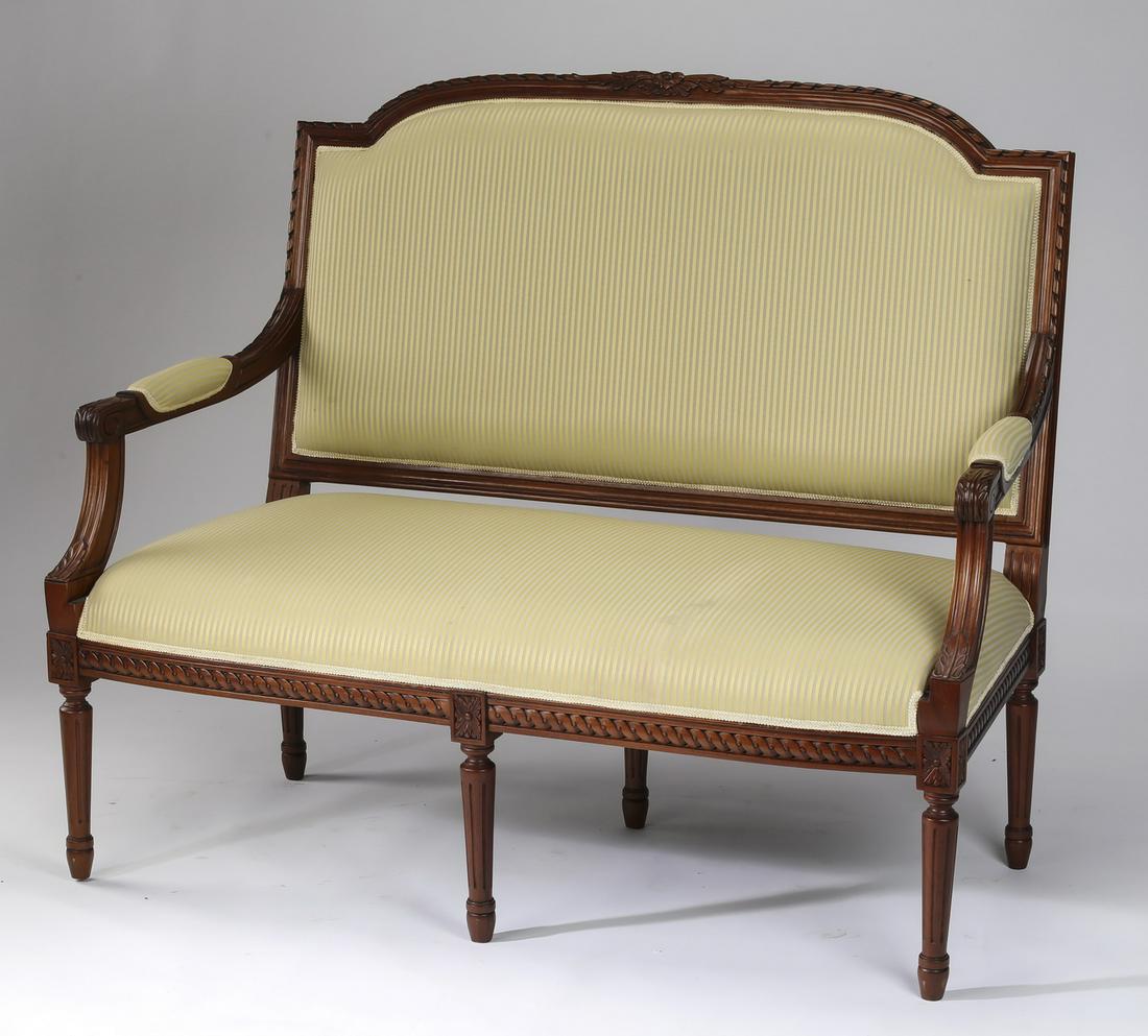 Louis XVI style mahogany settee: Louis XVI style mahogany settee, centering a carved floral crest on an arched ribbon carved crestrail, flowing into partially upholstered arms, flanking a bench seat upholstered in beige and celadon s