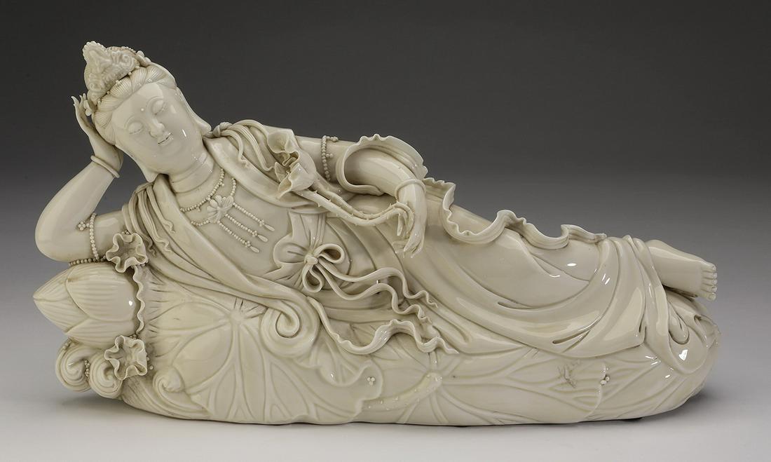 Chinese blanc de chine recumbent Quan Yin, 16"l: Chinese blanc de chine figure of Quan Yin, the goddess of mercy depicted reclining on a lotus leaf, wearing a crown and holding a lotus stem in one hand, 9"h x 16"l x 4"d.