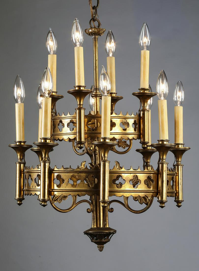Gothic style gilt metal 12-light chandelier: Continental gilt metal 12-light chandelier in the Gothic taste, having a two tiered circular frame pierced with quatrefoils, joined by foliate arms and interspaced with faux candles, 25"h x 19.5"d.