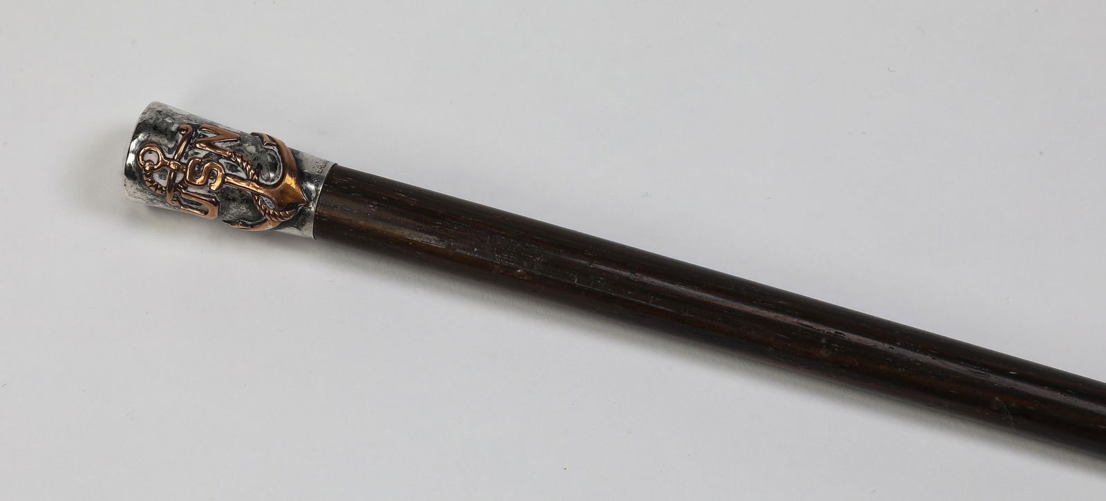US Naval swagger stick with sterling silver mount: Mixed metal military swagger stick, having a sterling silver knob tip with a copper 'USN' superimposed over an anchor, marked 'Sterling' surmounting a mahogany shaft terminating to a horn ferrule, 23.