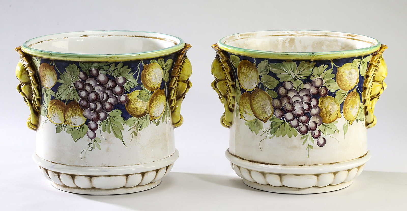 (2) Italian majolica planters w/fruits and lion masks: Pair of Italian majolica planters, crafted of glazed earthenware, of flared circular form, having a rim accented with clusters of lemons and grapes, flanked by paint-decorated lion masks, marked 'Made