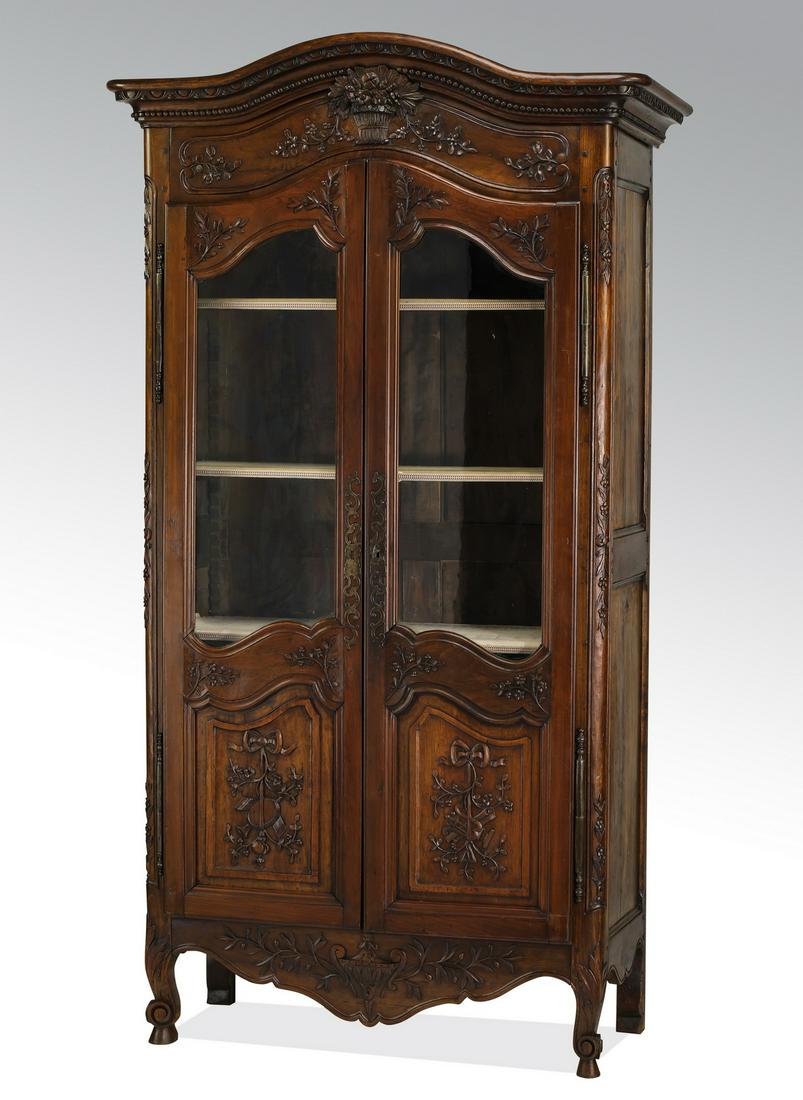 19th c. French Provincial style walnut vitrine: French Provincial style walnut vitrine, late 19th century, having an arched and molded cornice above the foliate basket medallion, flanked by relief carved garlands, rising on similarly carved doors w