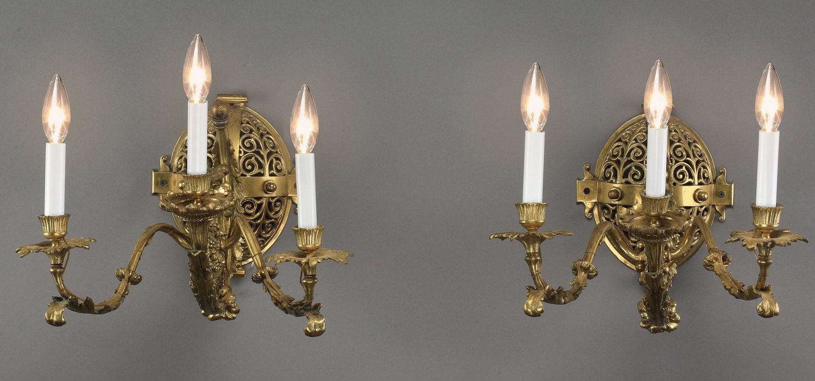 (2) Bronze Rococo Revival sconces, 10"h: Pair of bronze Rococo Revival style three light electrified sconces, each having an oval wall mount with a continuous scroll motif, issuing a scrolling acanthus arm, splitting into three acanthus 'S' 
