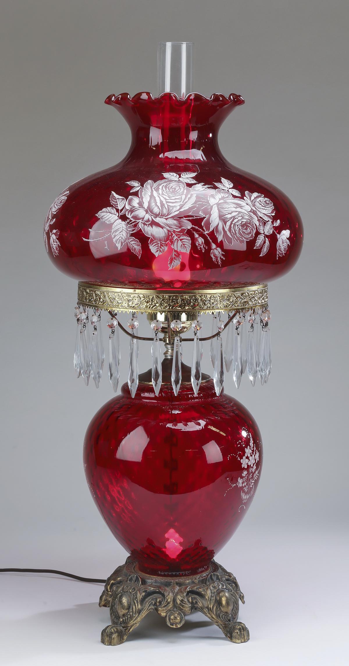 Ruby glass hurricane style table lamp, 32"h: Ruby glass 'Gone With the Wind' style table lamp, mid 20th century, of typical form with a compressed pomegranate shade decorated with hand painted white enamel rose sprays, resting on a brass collar